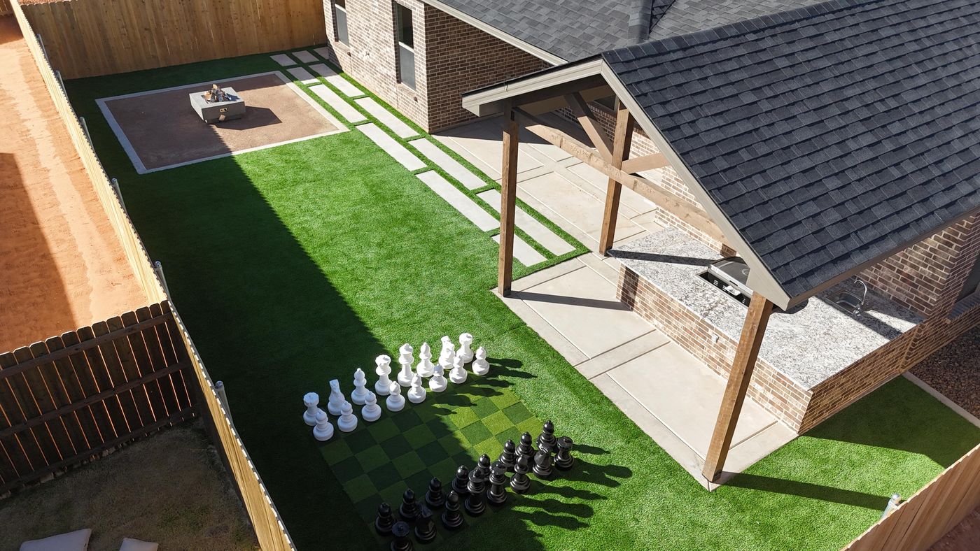 Aerial backyard with turf lawn, covered patio outdoor kitchen and giant lawn chess in Deer Meadows, Odessa TX