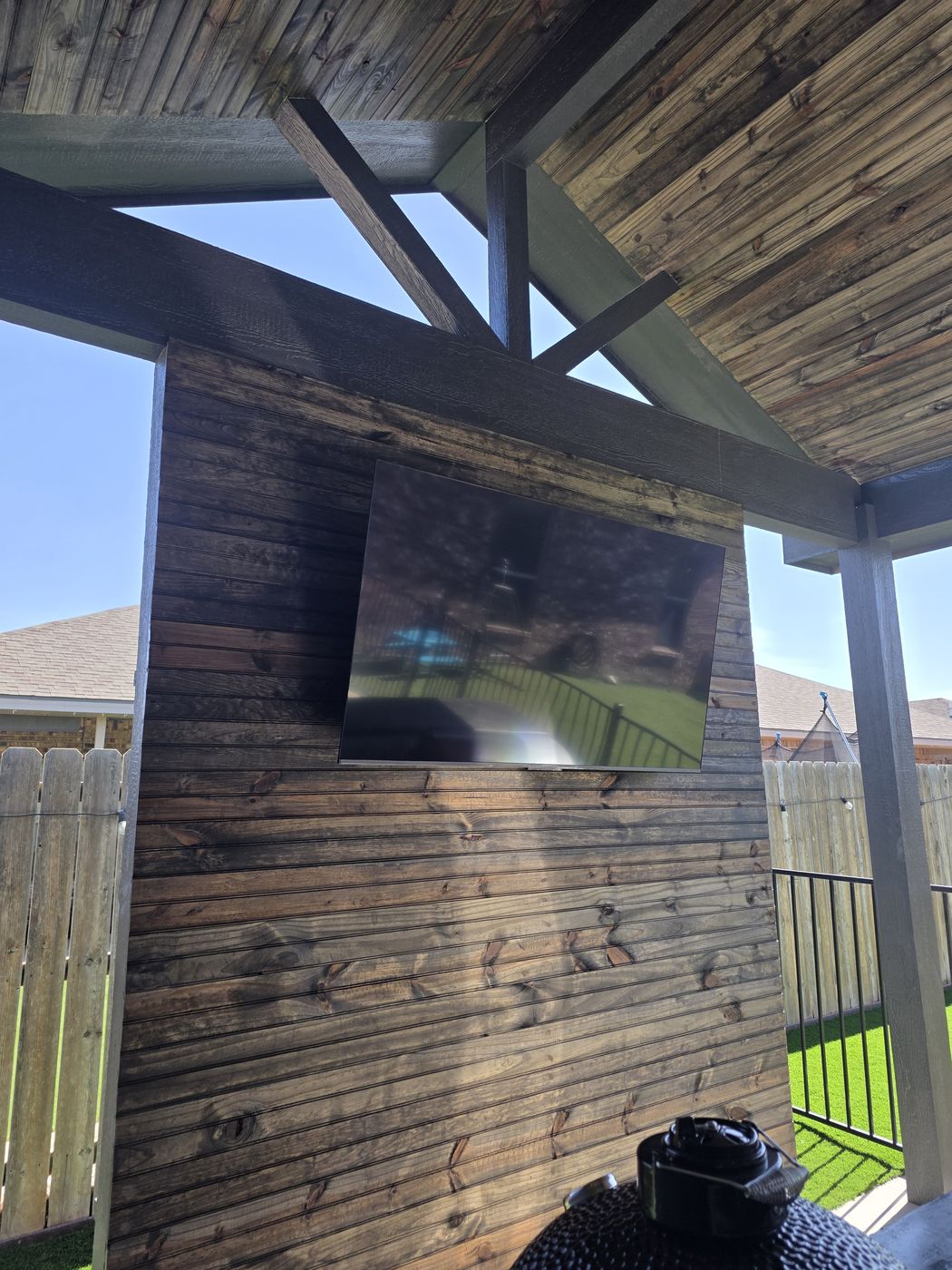 Stained tongue-and-groove patio ceiling with timber beams and mounted outdoor TV in Desert Ridge, Odessa TX