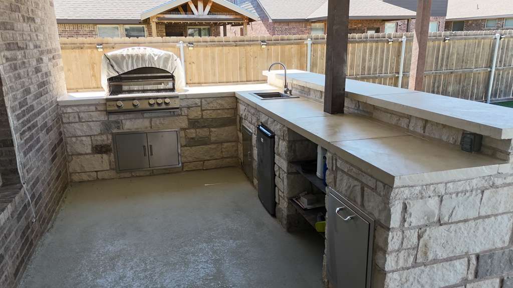 L-shaped limestone outdoor kitchen with concrete countertops, sink and bar seating in Desert Ridge, Odessa TX