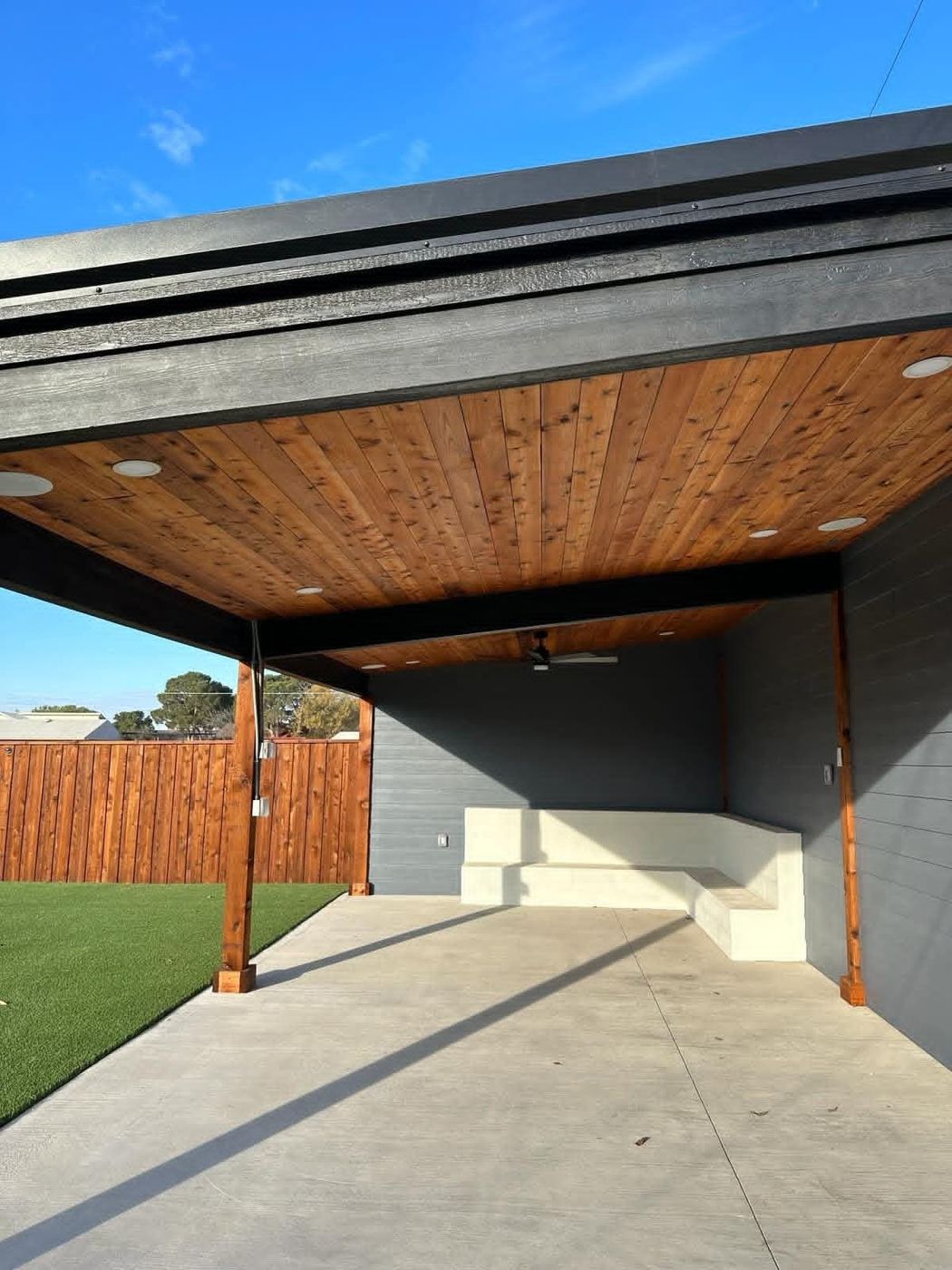 Modern shed-roof covered patio with cedar ceiling and floating concrete bench in Legacy South, Midland TX