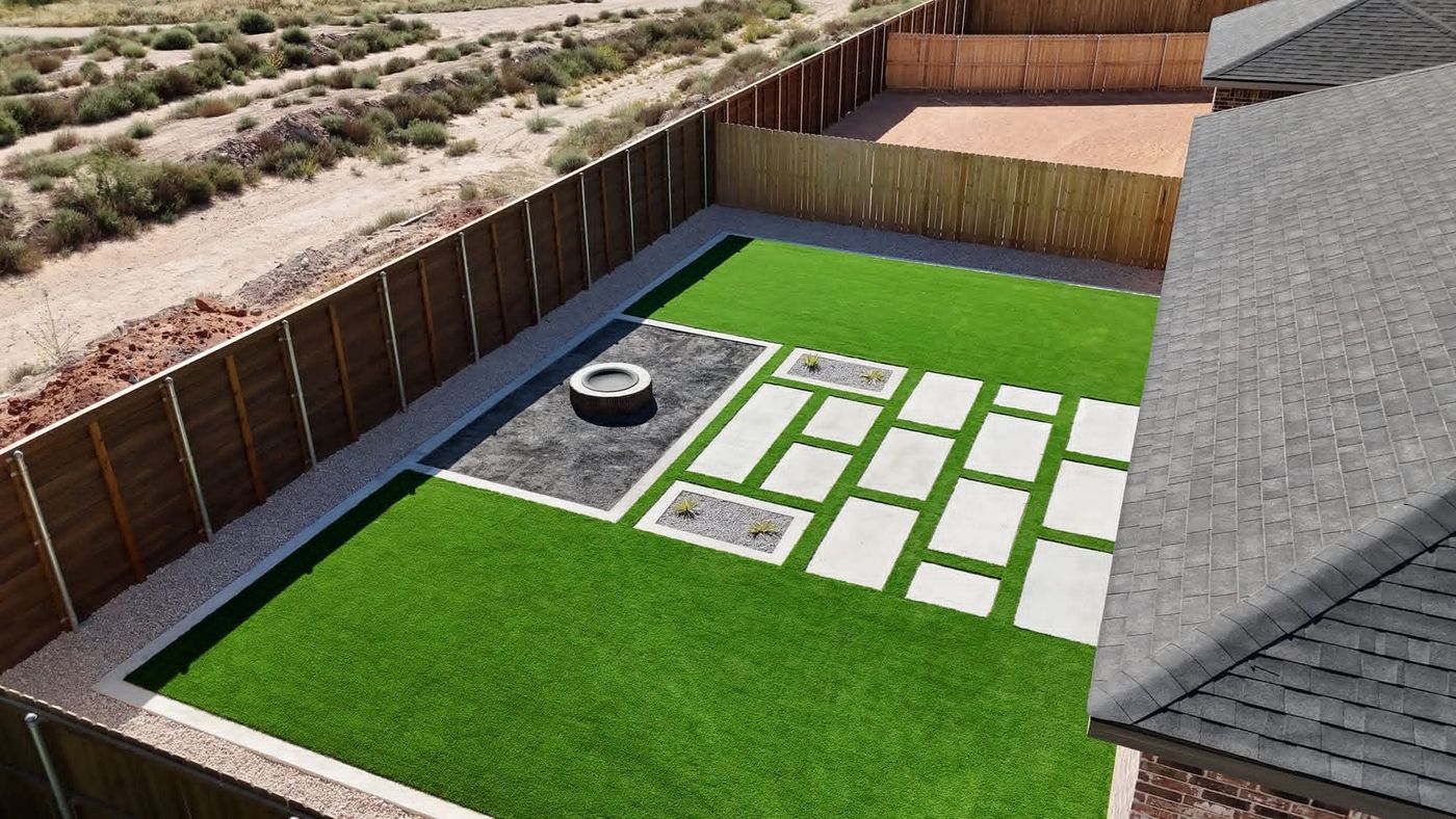 Aerial of artificial turf backyard with paver walkway, gravel inlays and round fire pit in Legacy South, Midland TX