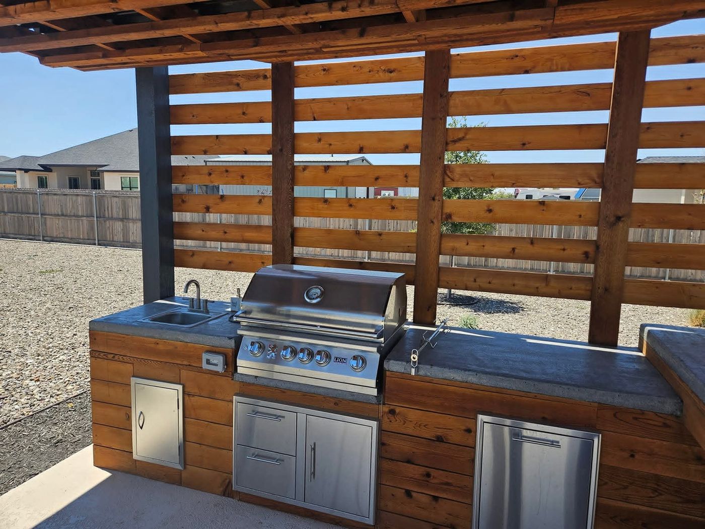 Custom outdoor kitchen under a cedar pergola with concrete countertop and stainless grill in Mockingbird Ridge, Midland TX