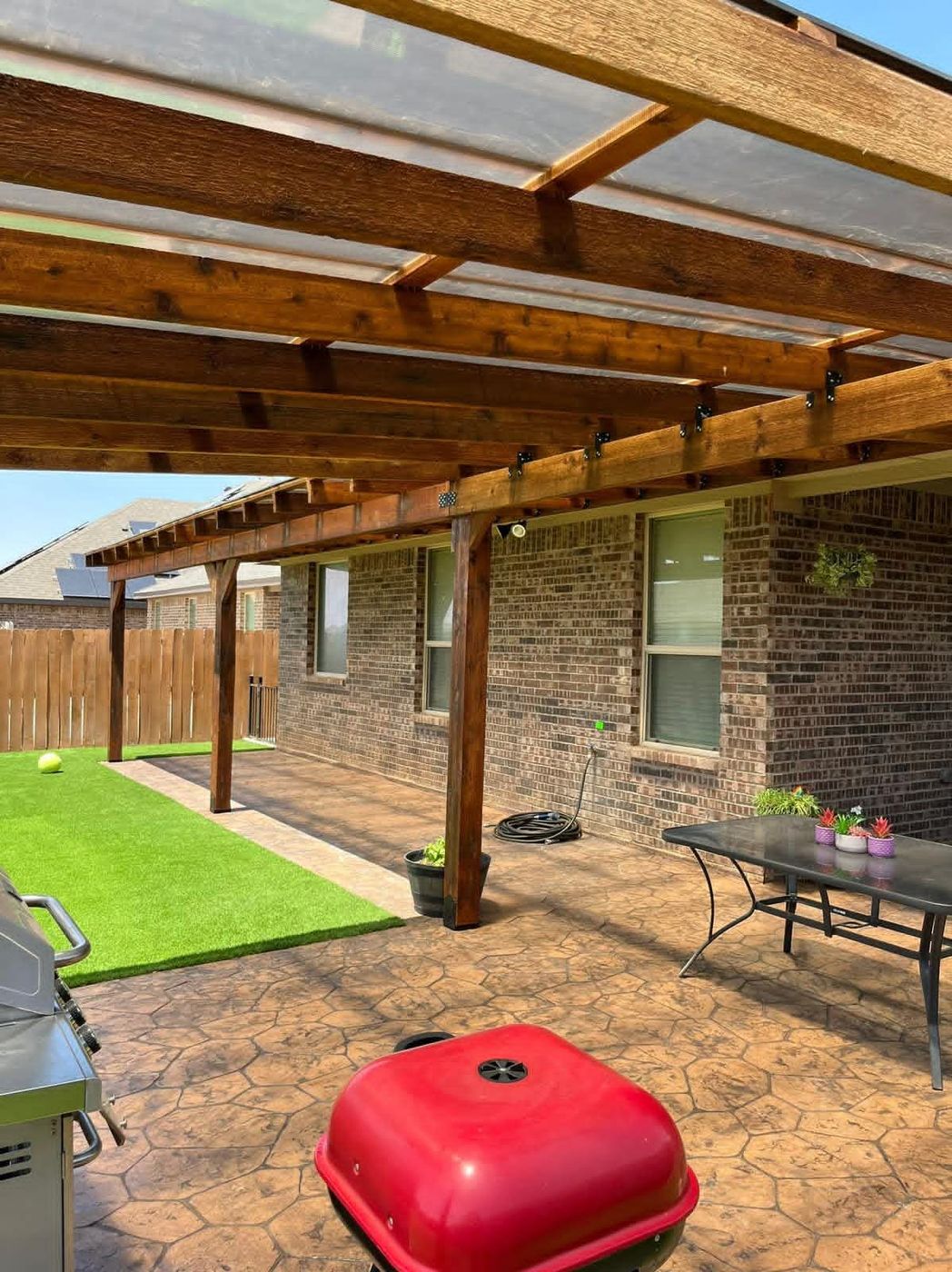 Cedar patio cover with clear polycarbonate roof panels over cobblestone stamped concrete in Pecan Grove, Midland TX